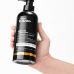 Рука держит чёрный флакон YOUtoo Keratin Nutrition Conditioner 500 мл — YOUtoo
