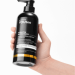 Рука держит чёрный флакон YOUtoo Keratin Nutrition Professional Repair Shampoo 500 мл — YOUtoo